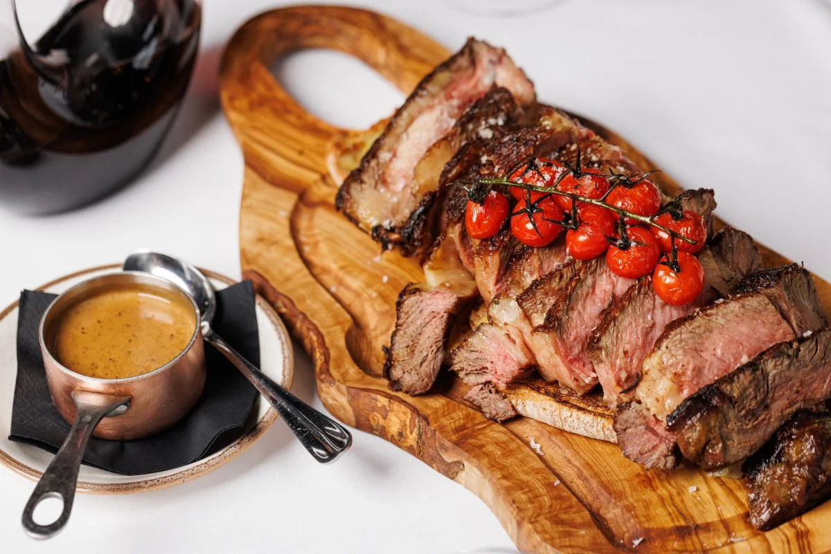 Tender sliced beef served on a wooden board with roasted tomatoes and sauce