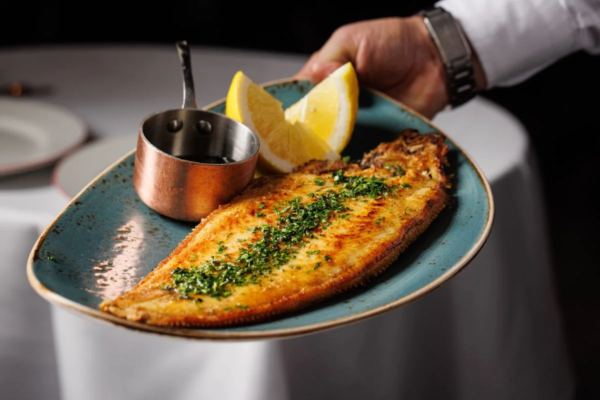 Golden grilled fish fillet with lemon wedges and sauce on a blue plate